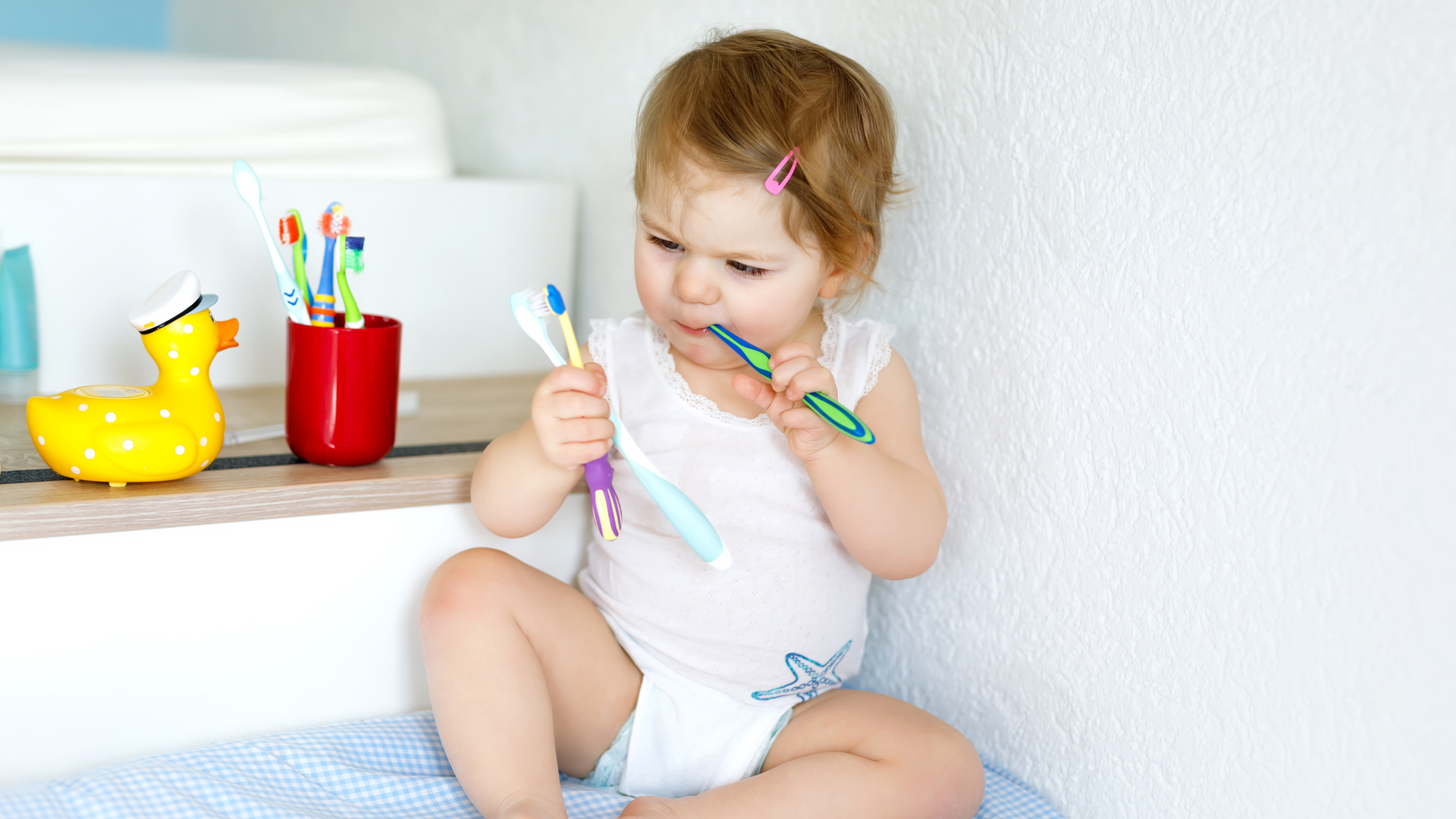 Little baby girl holding toothbrush and brushing first teeth. Toddler learning to clean milk tooth.