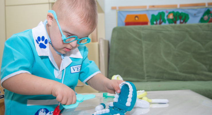 A boy with Down syndrome plays a role-playing game with dental toys and model