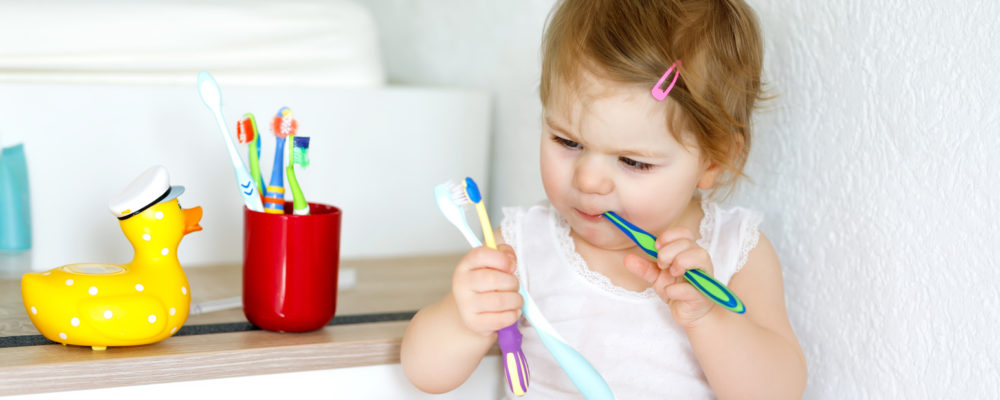 Little baby girl holding toothbrush and brushing first teeth. Toddler learning to clean milk tooth.