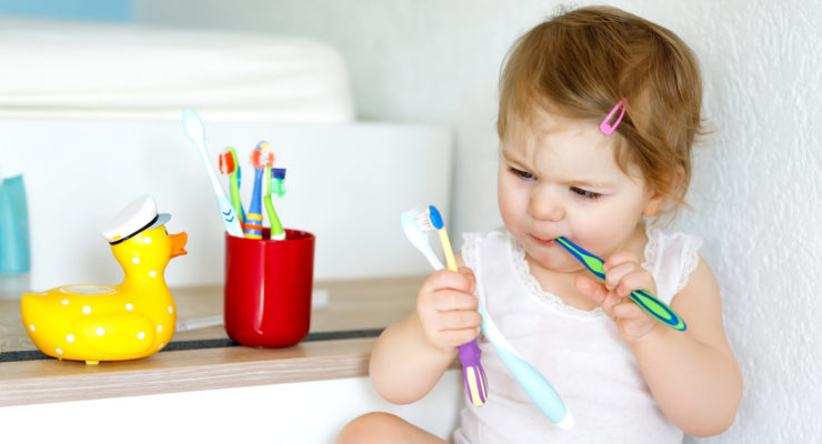 Little baby girl holding toothbrush and brushing first teeth. Toddler learning to clean milk tooth.