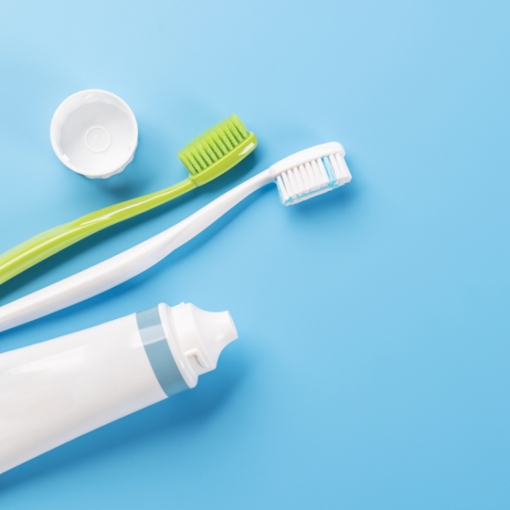 Two toothbrushes lie next to a toothpaste tube with its lid removed