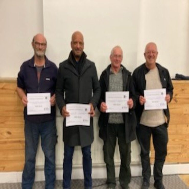 Four men in a row holding up certificates