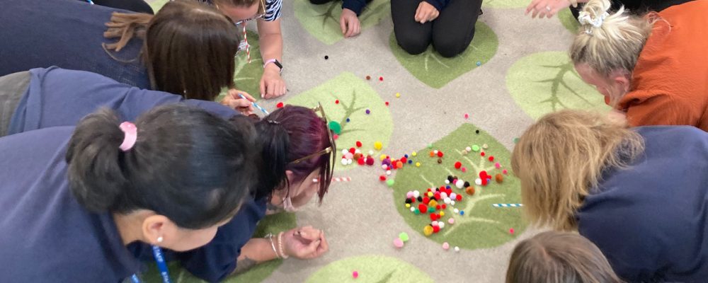 Nursery staff blowing pompoms across the floor using straws