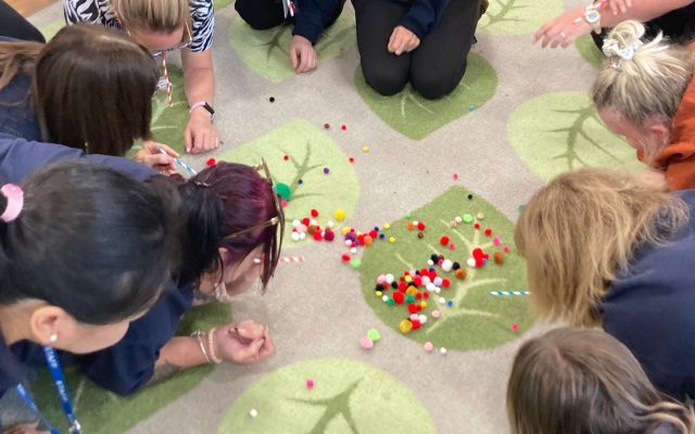 Nursery staff blowing pompoms across the floor using straws